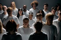 A diverse group of individuals stands together, emotionless, in a studio setting.